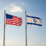 The American and Israeli flags flying side-by-side on tall flagpoles against a blue sky.